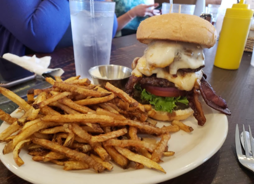 A towering burger with melted cheese, bacon, lettuce, and tomato, served with a side of crispy fries.