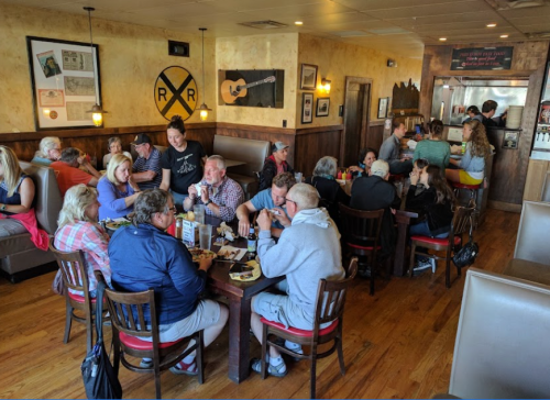 A busy restaurant scene with groups of people dining at tables, enjoying food and conversation in a cozy atmosphere.