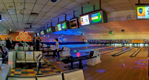 A vibrant bowling alley with colorful lights, multiple lanes, and screens displaying scores. People are enjoying bowling.