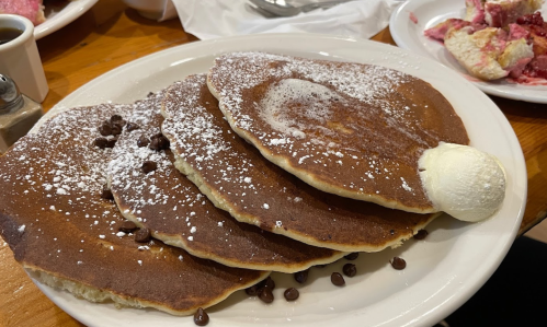 A plate of four fluffy pancakes topped with powdered sugar, chocolate chips, and a scoop of butter.