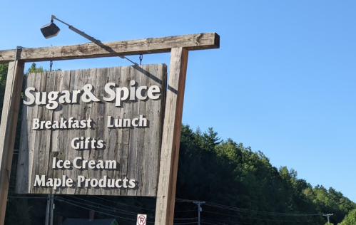 Sign for "Sugar & Spice" featuring breakfast, lunch, gifts, ice cream, and maple products against a clear blue sky.