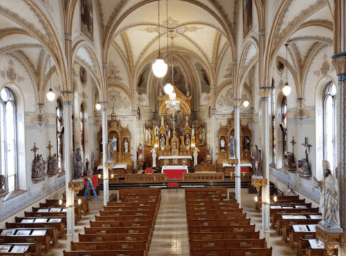Interior of a grand church featuring ornate architecture, wooden pews, and religious statues.