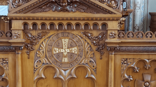 Intricate wooden altar with carvings, featuring a central emblem with letters and decorative elements.