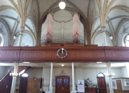 Interior of a church featuring a large pipe organ, wooden balcony, and decorative arches.