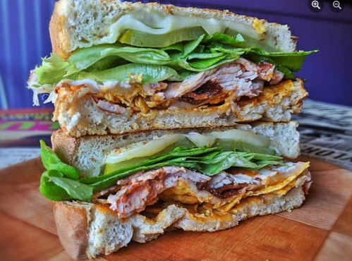 A close-up of a layered sandwich with turkey, lettuce, pickles, and mayonnaise on toasted bread, cut in half.