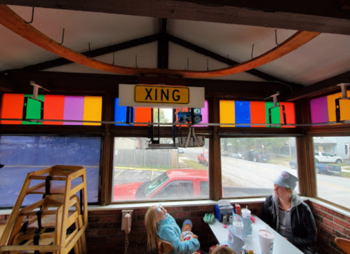 A colorful indoor space with a "XING" sign, tables, and a woman sitting with a child.