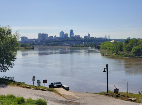 A serene river view with a city skyline in the background, clear blue sky, and green trees along the shore.