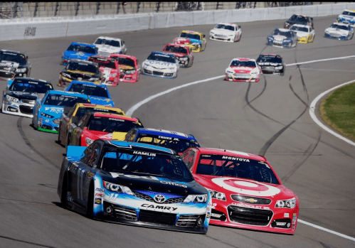 A group of NASCAR cars racing on a track, with one car in the foreground leading the pack.