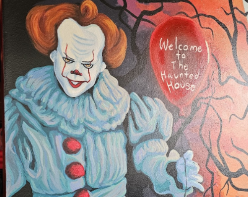 A colorful clown with red balloons stands against a spooky background, holding a sign that says "Welcome to The Haunted House."