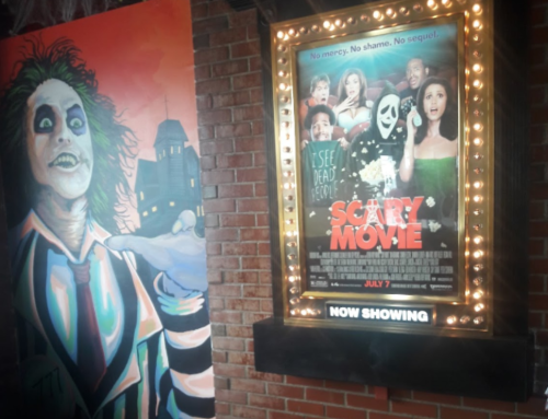 A movie poster for "Scary Movie" displayed in a theater, alongside a colorful mural of a character.