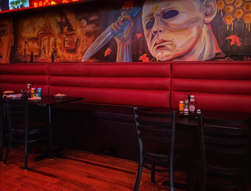 A dimly lit restaurant with red booths and a mural of a masked figure holding a knife on the wall.