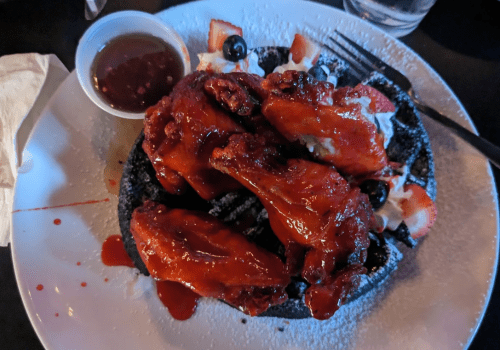 A plate of crispy chicken wings drizzled with sauce, served on a bed of whipped cream and topped with strawberries and blueberries.