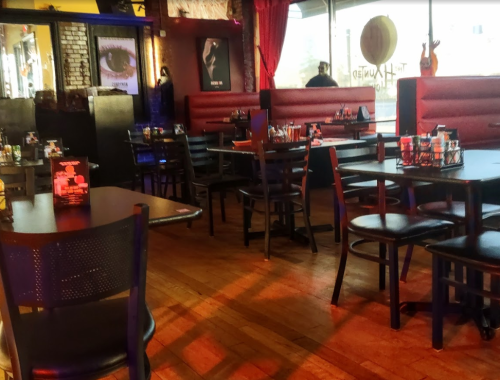 Interior of a restaurant with wooden floors, red booths, and tables set for dining. Warm lighting creates a cozy atmosphere.