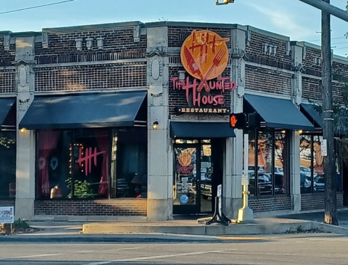 Exterior of "The Haunted House Restaurant," featuring a brick facade and large windows with a spooky-themed sign.