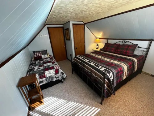 Cozy attic bedroom with a double bed, twin bed, and plaid bedding, featuring sloped ceilings and warm lighting.