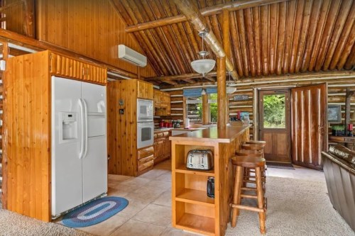 Cozy wooden kitchen with a bar, white appliances, and a rustic feel, featuring a door leading to the outdoors.