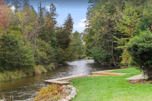 A serene river flows through a lush green landscape, surrounded by trees and a wooden platform by the water's edge.