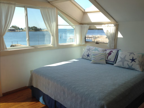 Bright bedroom with a large window overlooking a waterfront view, featuring a bed with decorative pillows.