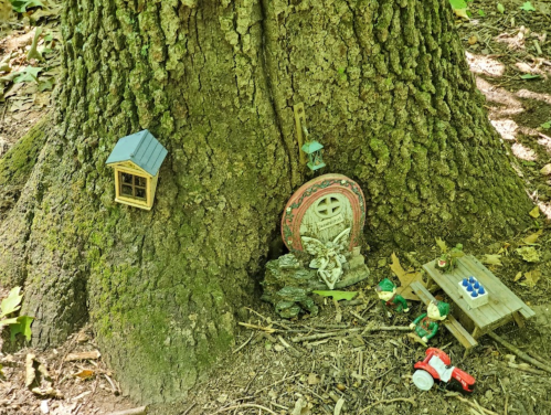 A whimsical scene at the base of a tree featuring a tiny house, a decorative door, and small figurines with a toy tractor.