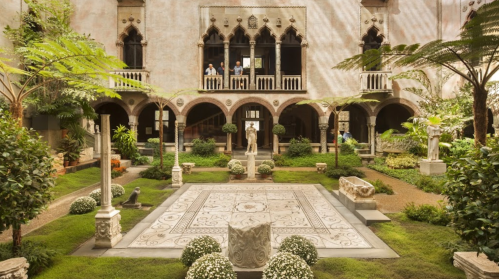 A serene courtyard garden with greenery, sculptures, and a patterned stone floor, surrounded by ornate architecture.