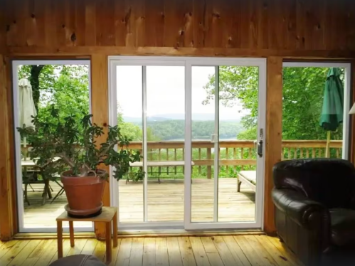 A cozy interior view through sliding glass doors, showcasing a wooden deck and lush green landscape outside.