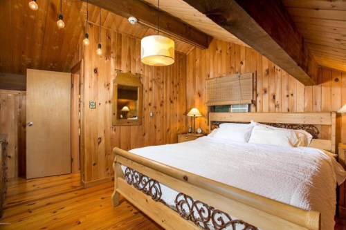 Cozy wooden bedroom with a large bed, warm lighting, and rustic decor, featuring a mirror and wooden accents.