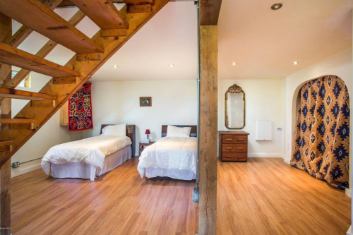 Cozy room with two single beds, wooden floors, a staircase, and decorative curtains.