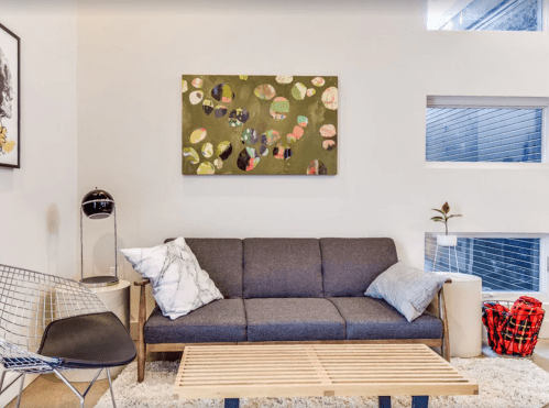 A modern living room featuring a gray sofa, a wooden coffee table, and abstract wall art above.