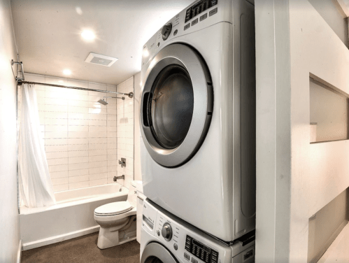 A compact laundry area featuring a stacked washer and dryer next to a bathroom with a bathtub and toilet.