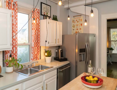 Bright kitchen with white cabinets, a gray fridge, and a wooden island, featuring plants and decorative lighting.