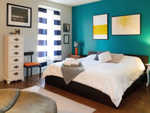 A cozy bedroom with a large bed, colorful walls, striped curtains, and stylish decor.