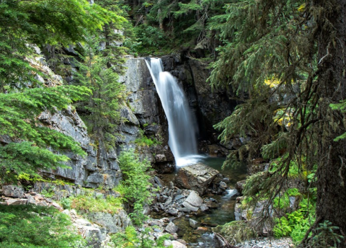A serene waterfall cascades down rocky cliffs, surrounded by lush green trees and foliage.