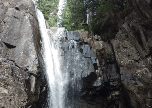 A waterfall cascading down rocky cliffs, surrounded by lush green trees and a clear blue sky.
