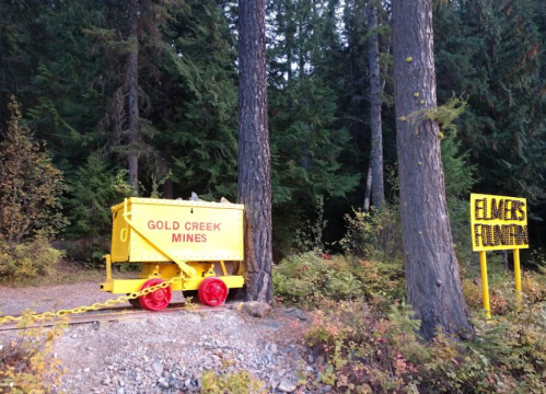 A yellow mining cart labeled "Gold Creek Mines" next to a sign in a forested area.