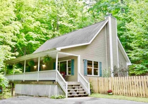 A charming house surrounded by lush greenery, featuring a front porch and wooden steps leading to the entrance.