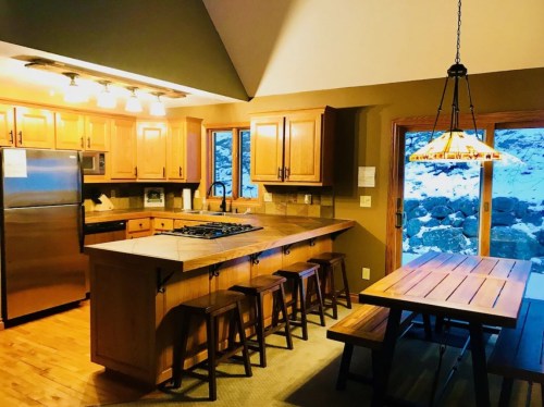 Cozy kitchen with wooden cabinets, a gas stove, and a dining area featuring a wooden table and chairs, with snowy views outside.