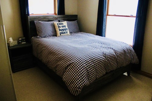 Cozy bedroom featuring a checkered bedspread, decorative pillow, and large windows with natural light.
