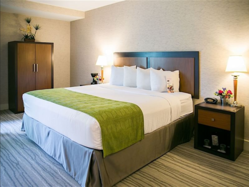 A cozy hotel room featuring a king-sized bed with green accents, nightstands, and a wardrobe. Soft lighting creates a warm ambiance.