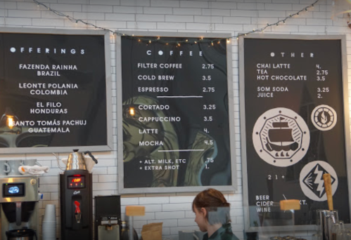 Menu board displaying coffee and other drink offerings with prices, set in a cozy café environment.