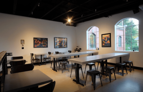 A spacious, modern café with tables, chairs, and colorful artwork on the walls, featuring large windows.