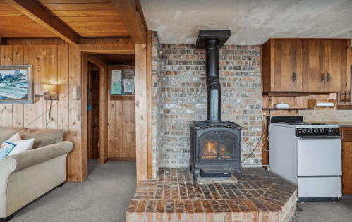 Cozy interior featuring a wood stove, brick hearth, and wooden cabinetry in a rustic living space.