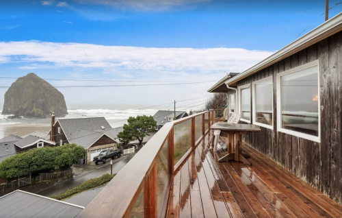 A coastal view from a wooden deck, overlooking the ocean and a large rock formation under a cloudy sky.