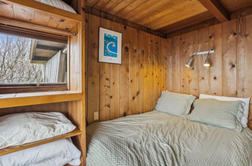 Cozy wooden bedroom with a double bed, decorative pillows, and a window letting in natural light.