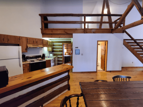 Cozy cabin interior featuring a kitchen, dining area, and loft with wooden beams and rustic decor.