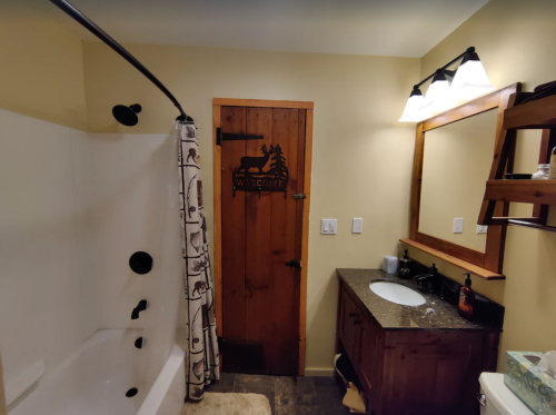 A cozy bathroom featuring a shower, wooden door with a welcome sign, and a dark countertop with a mirror.