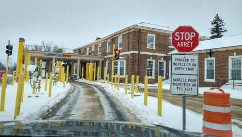A snowy border checkpoint with a stop sign and traffic lights, leading to an inspection area.