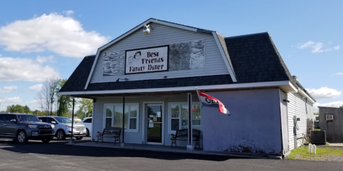 Exterior of "Best Friends Family Diner," featuring a sign, open flag, and benches outside on a sunny day.