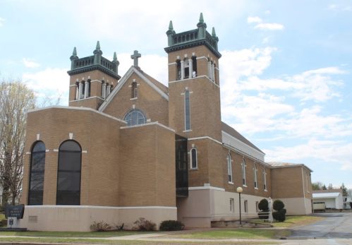 A large brick church with two tall towers and a cross on top, set against a partly cloudy sky.