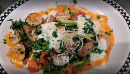 A colorful plate of shrimp, vegetables, and herbs, topped with creamy sauce and garnished with parsley.