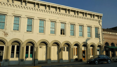 Historic brick building with arched windows and doors, featuring a blue sky in the background.